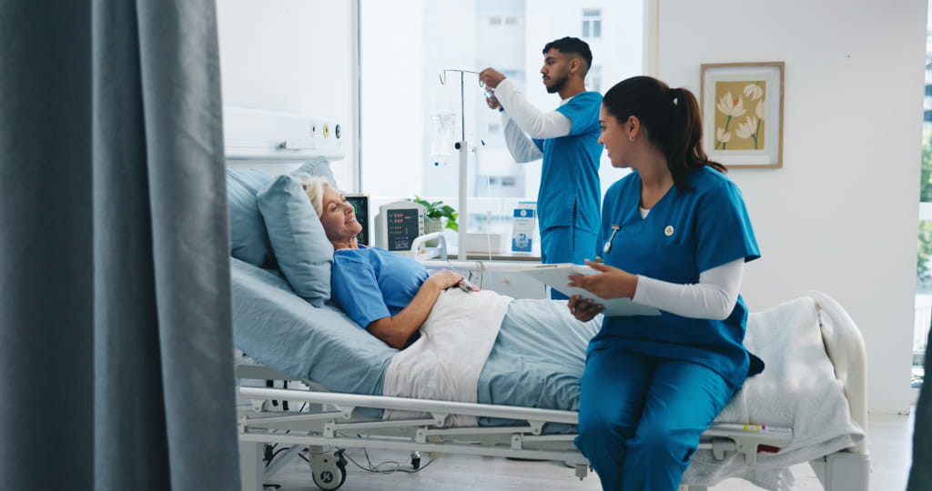 Zwei Pflegekräfte betreuen eine Patientin in einem modernen Krankenhauszimmer